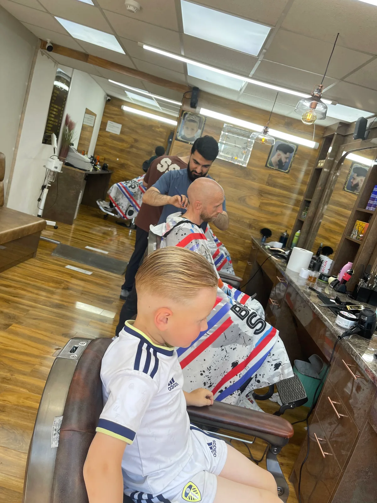A young customer's finished haircut with the Cutting Crew barbers at work behind him
